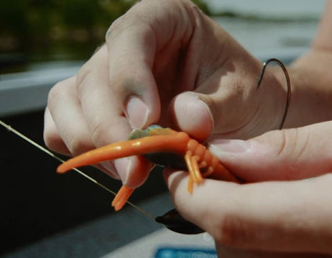 A close-up shot of a fisherman putting a hook into a an orange fishing lure and a BaitCloud inSert